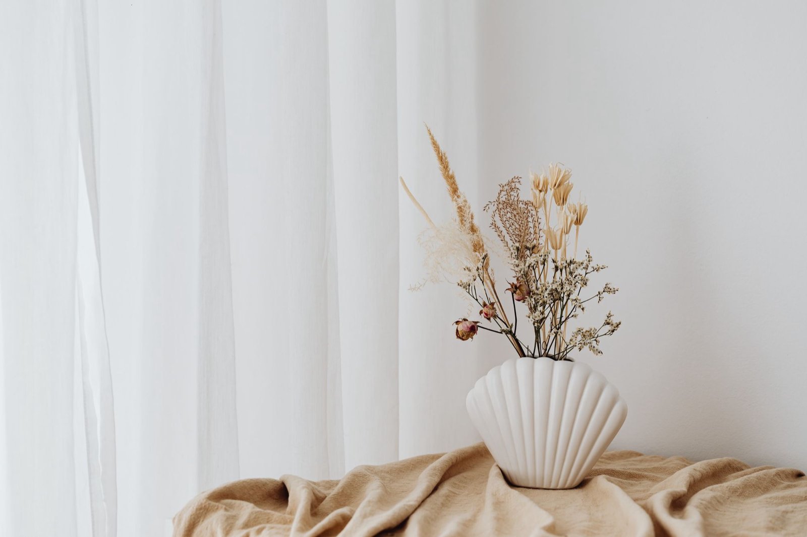 Dried flowers in a shell-shaped vase on soft cream linen
