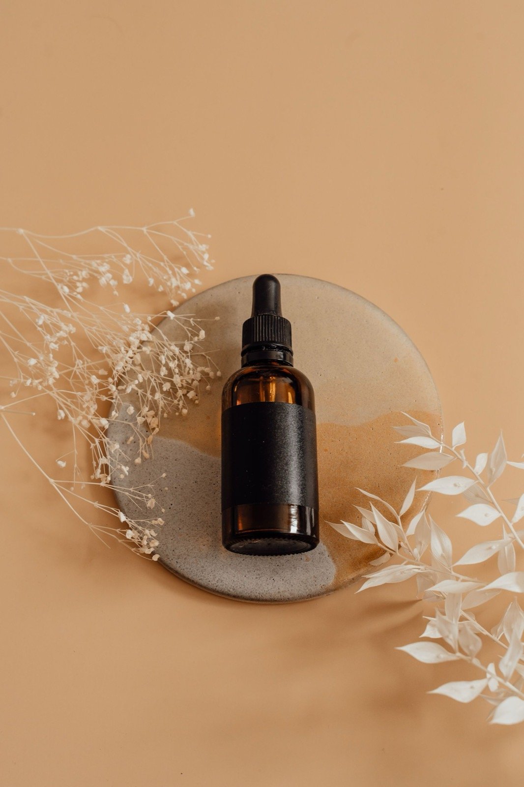 Amber dropper bottle with dried flowers on a warm peach background