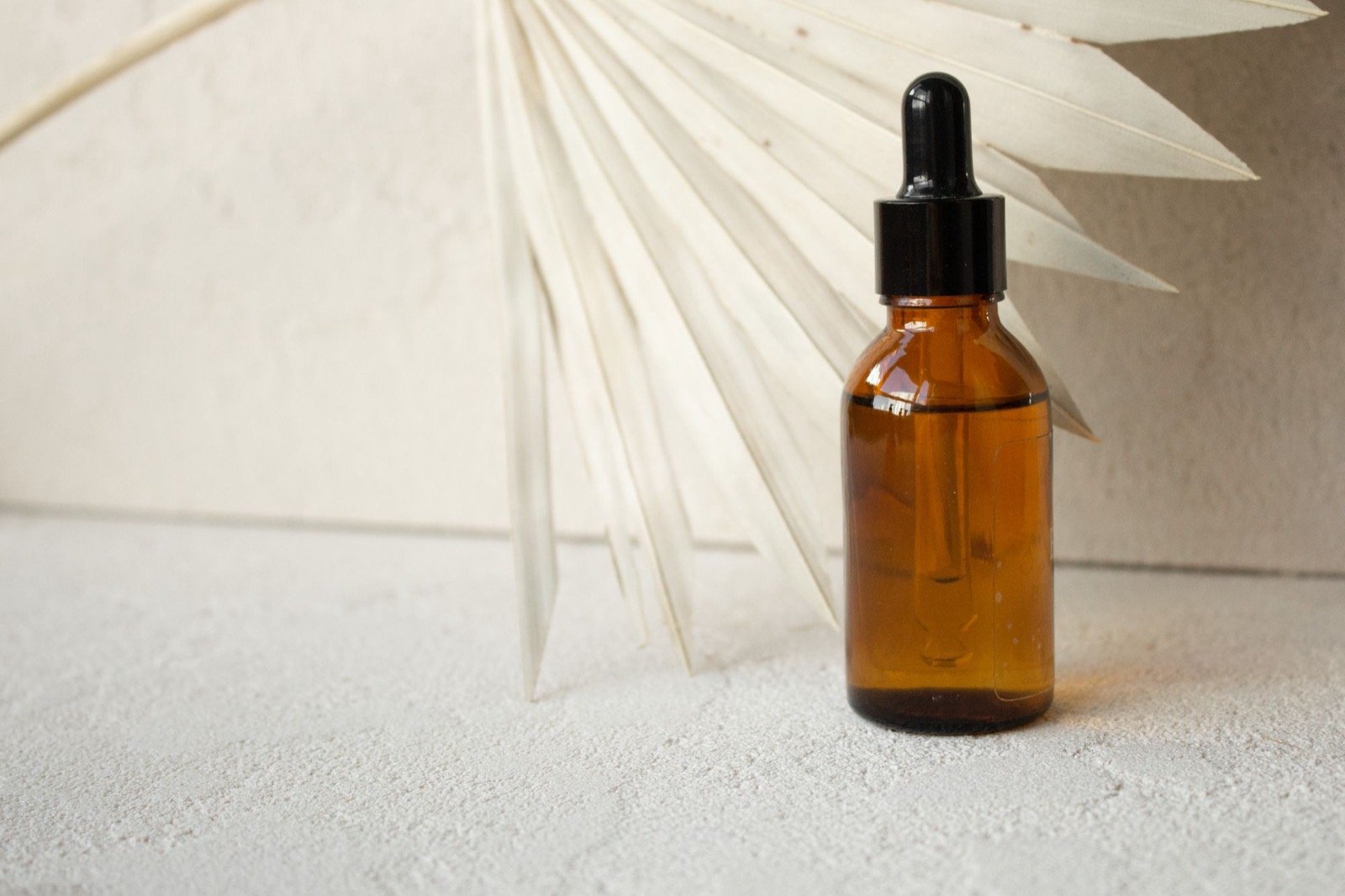 Amber serum bottle beside a dried palm leaf on cream linen